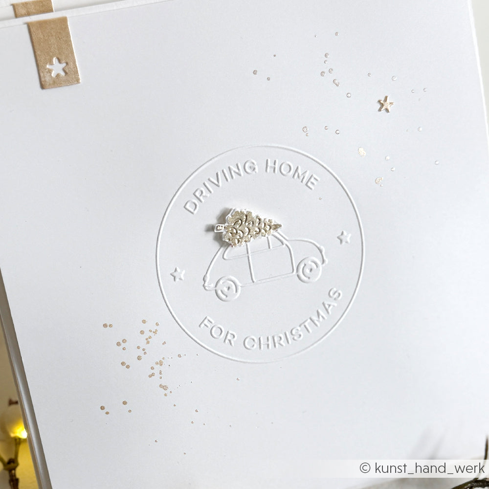 Weiße Karte von Alexandra Renke mit geprägtem Auto mit Weihnachtsbaum und dem Text "Driving Home For Christmas", erstellt mit dem Cut & Emboss Folder für festliche Textur und Charme.