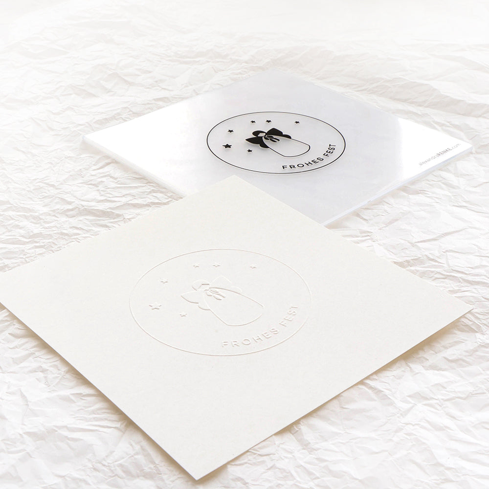 Zwei quadratische Karten von Alexandra Renke - eine durchsichtig, eine weiß - zeigen "Frohes Fest" mit einer Glocke und Sternen, die mit einem Prägefolder für subtile Textur und minimalistische Eleganz gestaltet wurden.