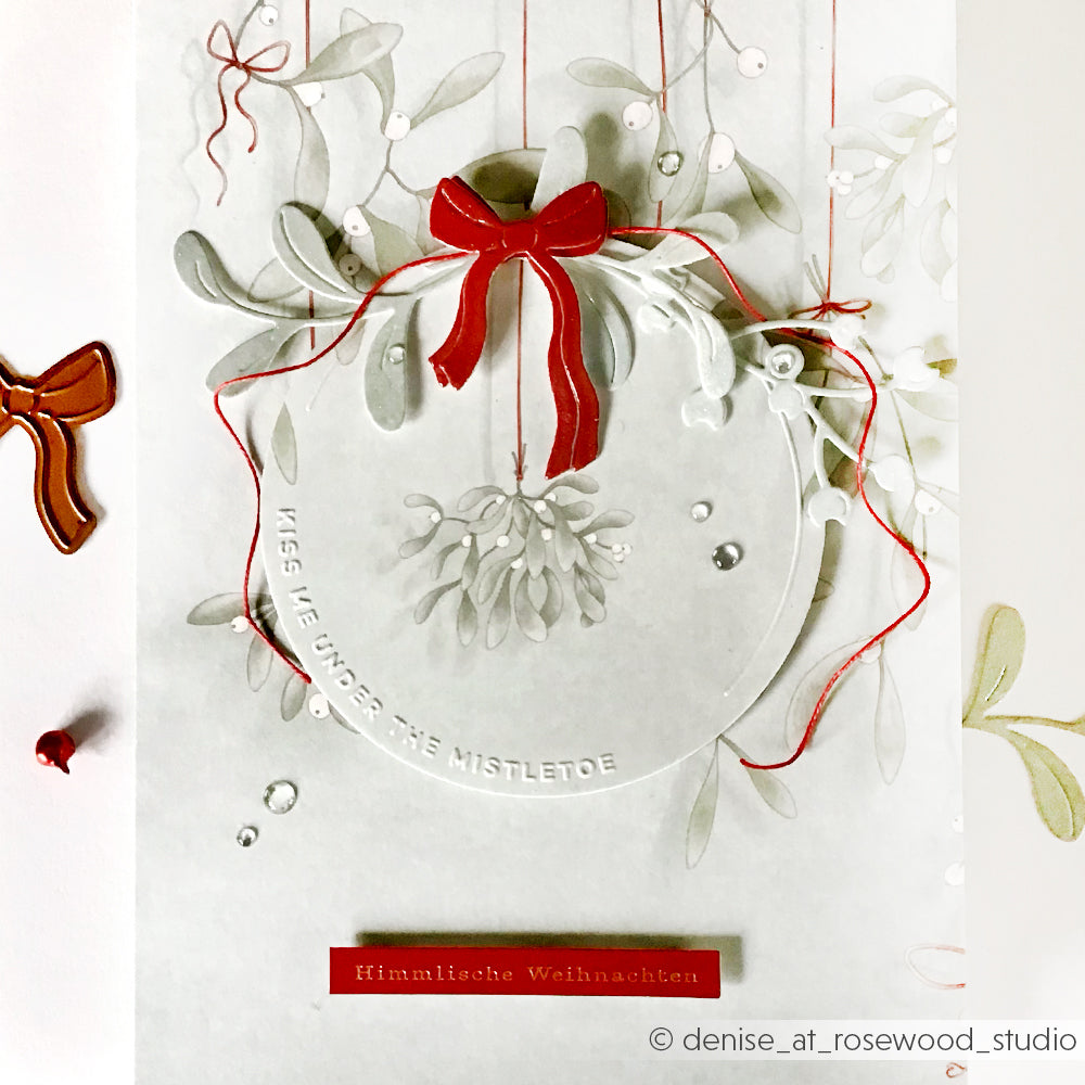 Weiße Karte von Alexandra Renke mit roter Schleife, Mistelzweig-Illustration und "Himmlische Weihnachten" in Rot - ideal, um Ihre Lieblingsmotive aus dem Embossing Folder oder den DieCut Systemen zu verwenden.
