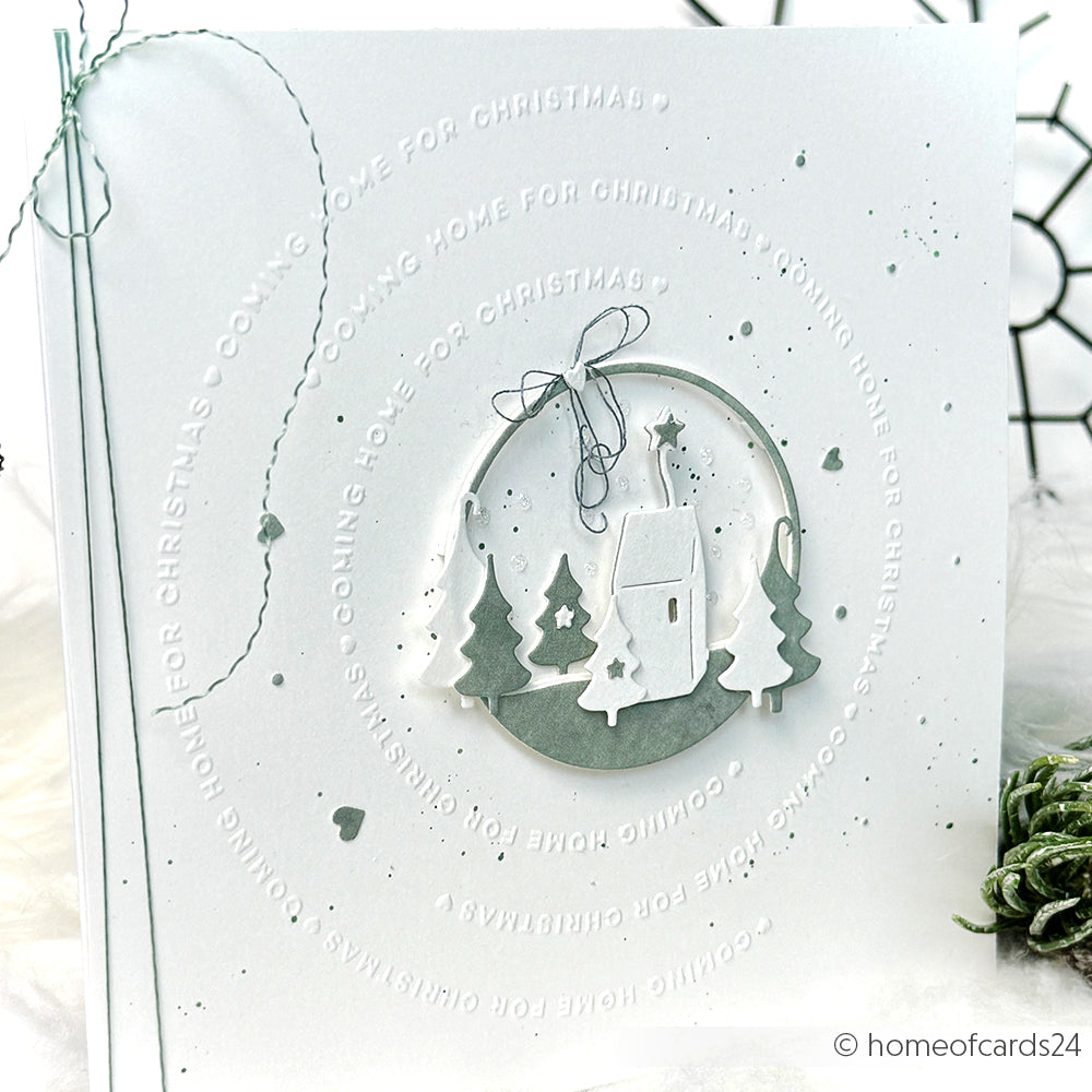 Weiße Weihnachtskarte von Alexandra Renke mit geprägtem Text "Coming home for Christmas" und einer ausgeschnittenen Winterdorfszene in der Mitte, erstellt mit einem Cut & Emboss Folder.