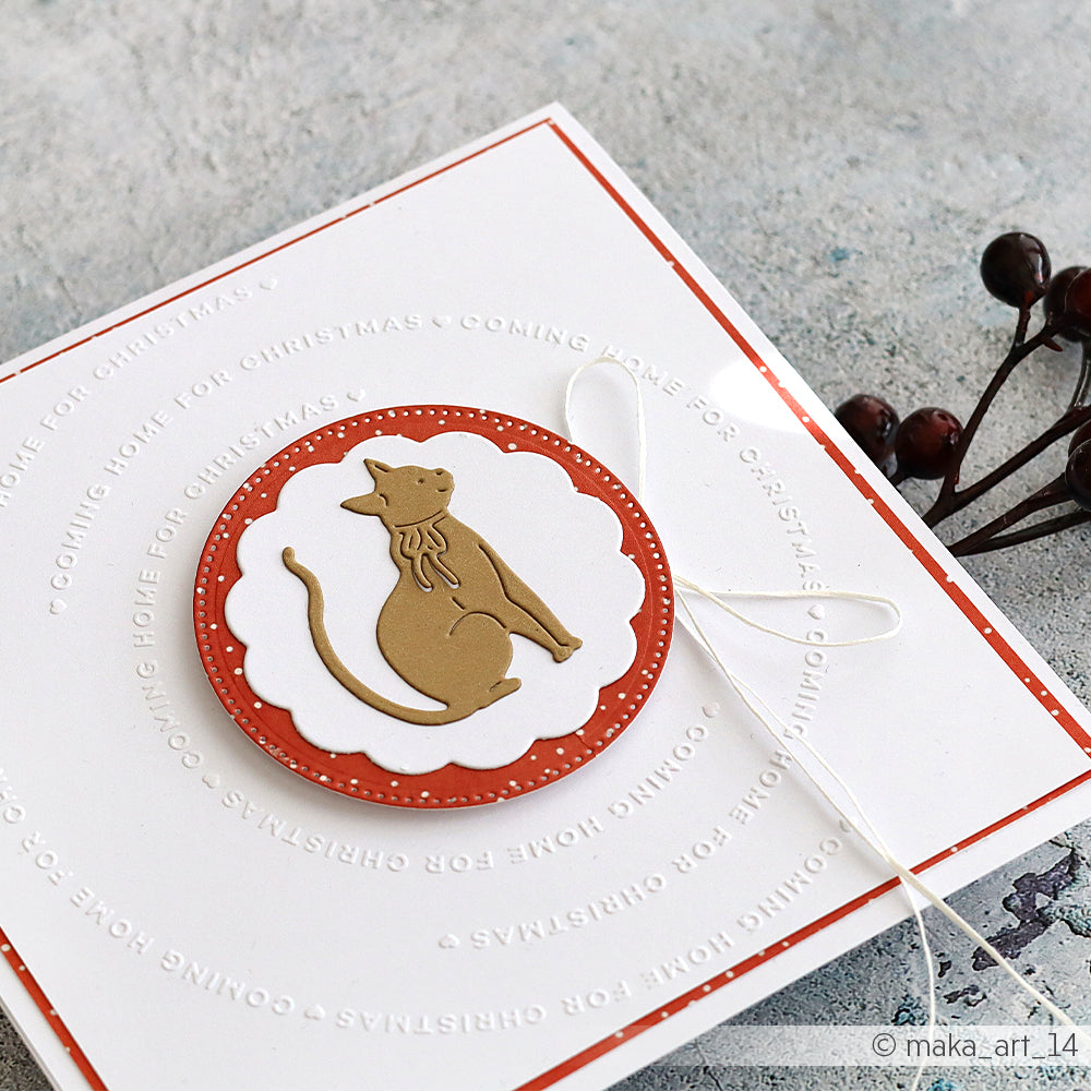Handgefertigte Weihnachtskarte von Alexandra Renke mit einer goldenen Katzensilhouette auf einem rot-weißen Kreis, verziert mit einer weißen Schleife. Erstellt mit dem Cut & Emboss Folder für dimensionale Textur.