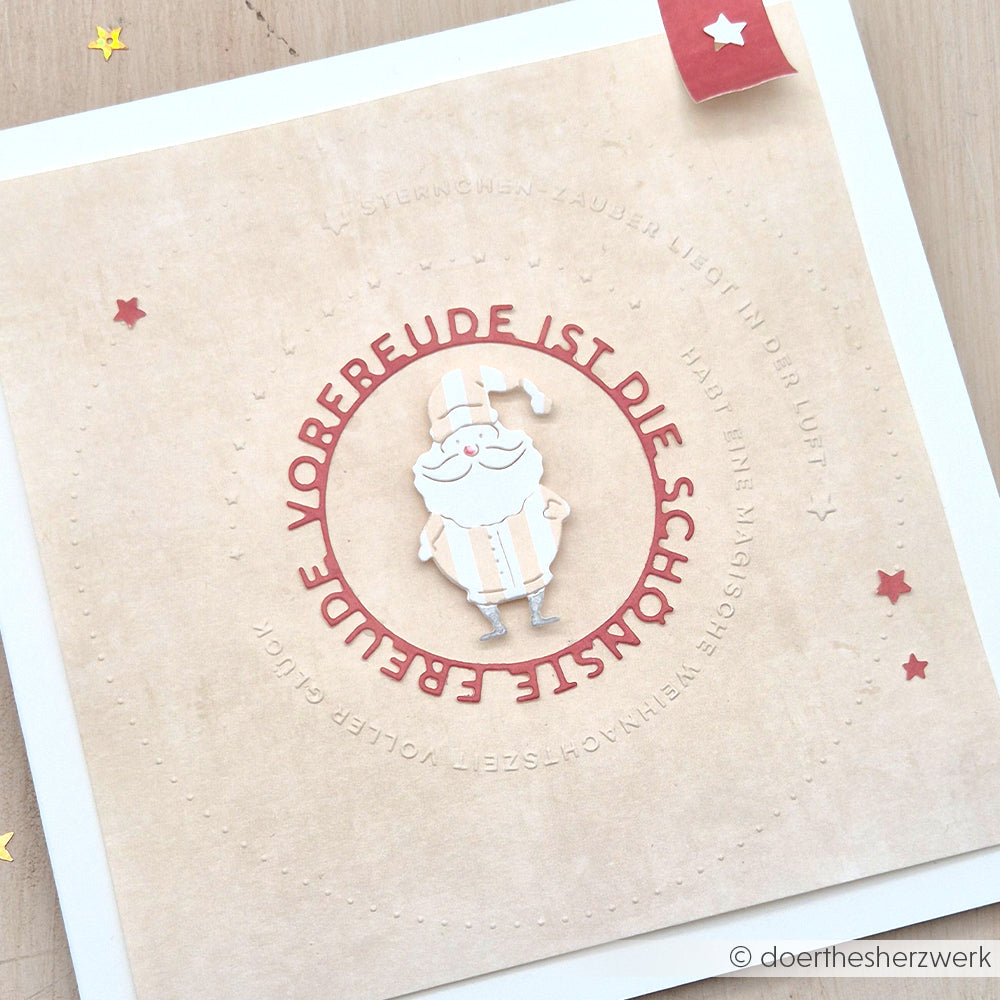 Handgefertigte Karte mit einer Weihnachtsmann-Illustration und deutschem Text in einem roten Kreis, hergestellt mit dem Alexandra Renke Typo Kreis Sternchen-Zauber Prägefolder für festliche Textur und Details.