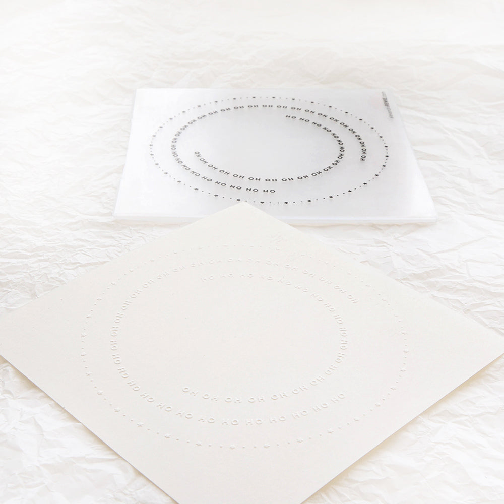 Zwei quadratische Bögen mit konzentrischen Kreisen und den Wörtern ON und NO, die mit dem Prägefolder Typo Kreis Ho Ho Ho von Alexandra Renke hergestellt wurden, liegen auf einem zerknitterten weißen Hintergrund.
