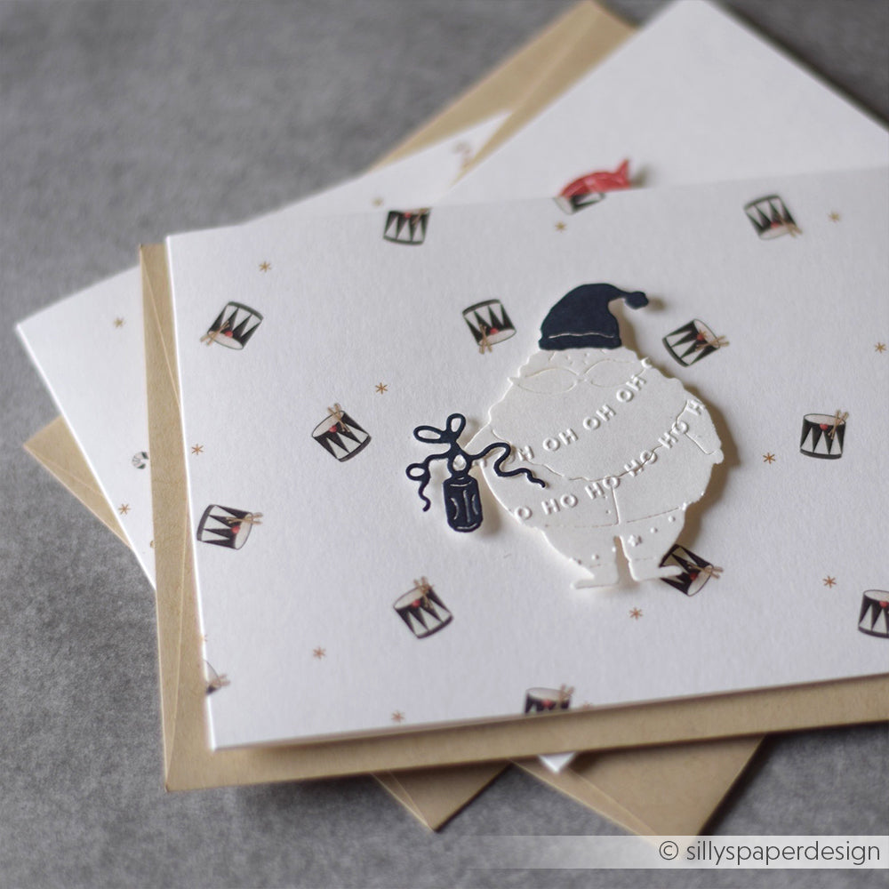Eine festliche Karte von Alexandra Renke mit einer Weihnachtsmann-Silhouette, kleinen Trommeln und "Oh oh oh, oh no presents!" auf grauem Hintergrund - wunderschön strukturiert mit einem Embossing Folder.