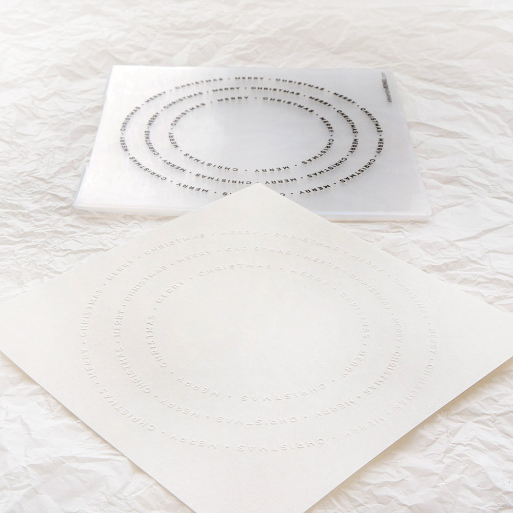 Zwei durchscheinende Alexandra-Renke-Bögen mit konzentrischen kreisförmigen "Typo Kreis Merry Christmas"-Textmustern, dargestellt auf geknittertem weißem Papier.