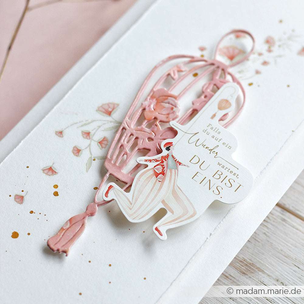 Rosa-weiße Karte von Alexandra Renke mit Zirkusfigur, Vogelkäfig und deutschem Text auf floralem Hintergrund - ideal für Papertie-Projekte oder als einzigartige Ephemera beim kreativen Basteln.