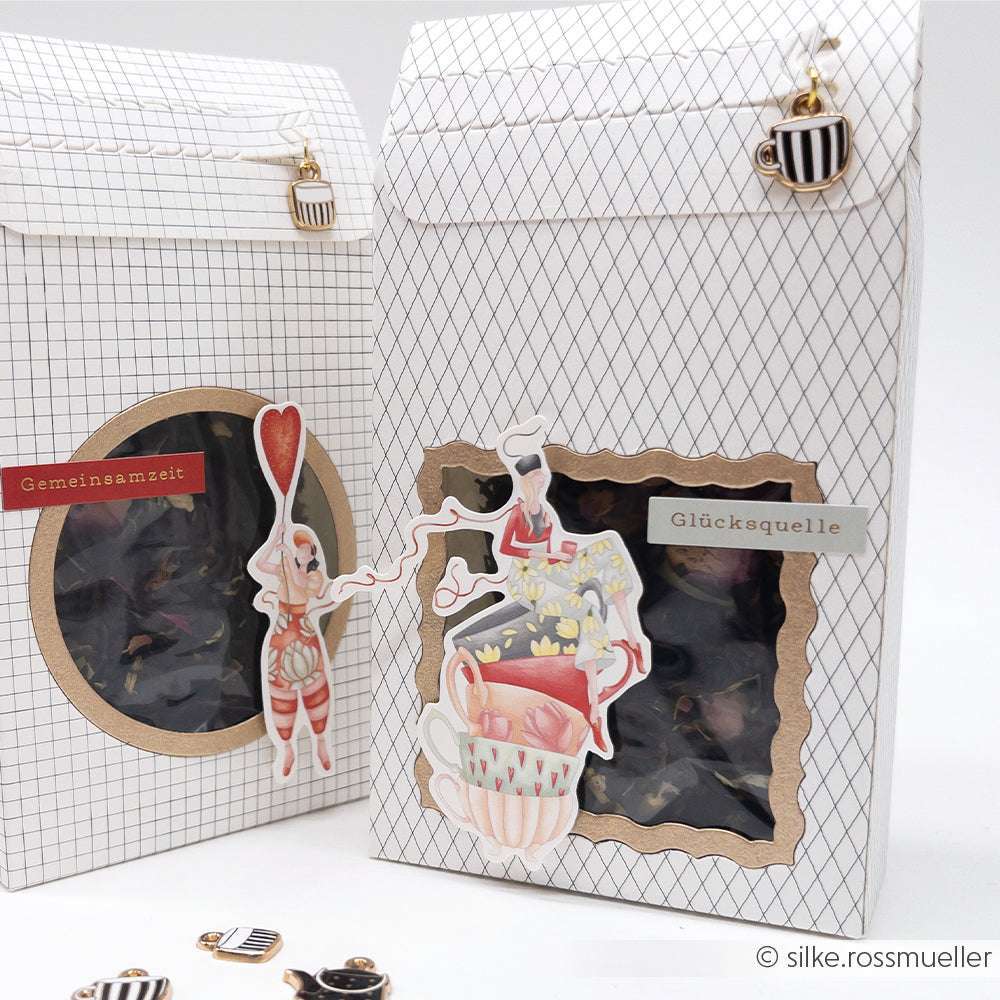 Zwei dekorierte Alexandra Renke Geschenktüten mit Kaffeetassen-Anhängern, skurriler Kunst, deutschen Etiketten und charmanten Papierelementen auf weißem Hintergrund - ideal für Ihr nächstes Papercraft-Projekt oder Ihre Ephemera-Sammlung.