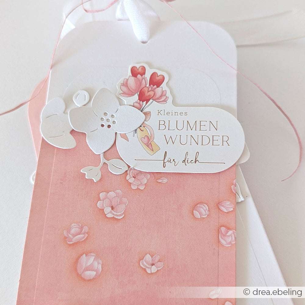 Geschenkanhänger von Alexandra Renke mit floralen Motiven, rosafarbenen Blütenblättern und dem Text "Kleines BLUMEN WUNDER für dich" auf rosafarbenem Hintergrund - ideal für Papertie-Projekte oder als charmante Papierelemente in Ephemera-Sammlungen.
