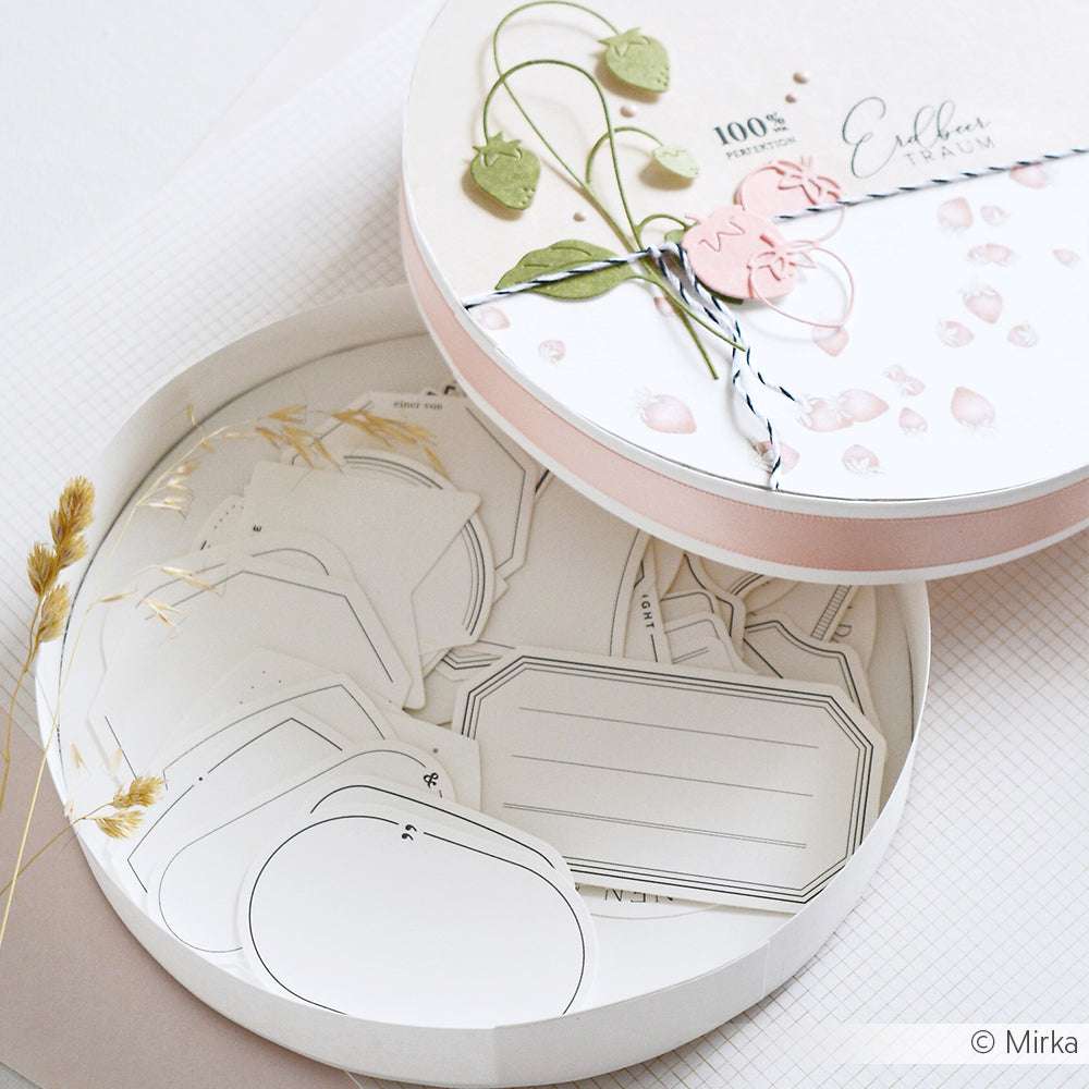 Alexandra Renke runde Schachtel mit botanischem Design, gefüllt mit verschiedenen Blanko-Papieranhängern, Karten und Ephemera - einige mit goldenen Akzenten - ideal für Papercraft-Projekte.