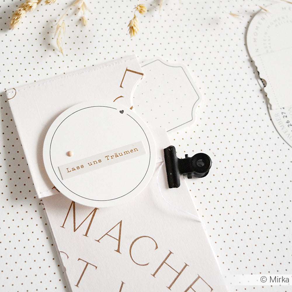 Die minimale Karte von Alexandra Renke zeigt "Lass uns Träumen" in deutscher Sprache auf einem weißen, runden Anhänger, der auf einem gepunkteten Hintergrund befestigt ist - perfekt für Papercraft-Projekte oder als einzigartige Ephemera und Papierelemente in Ihrer Sammlung.