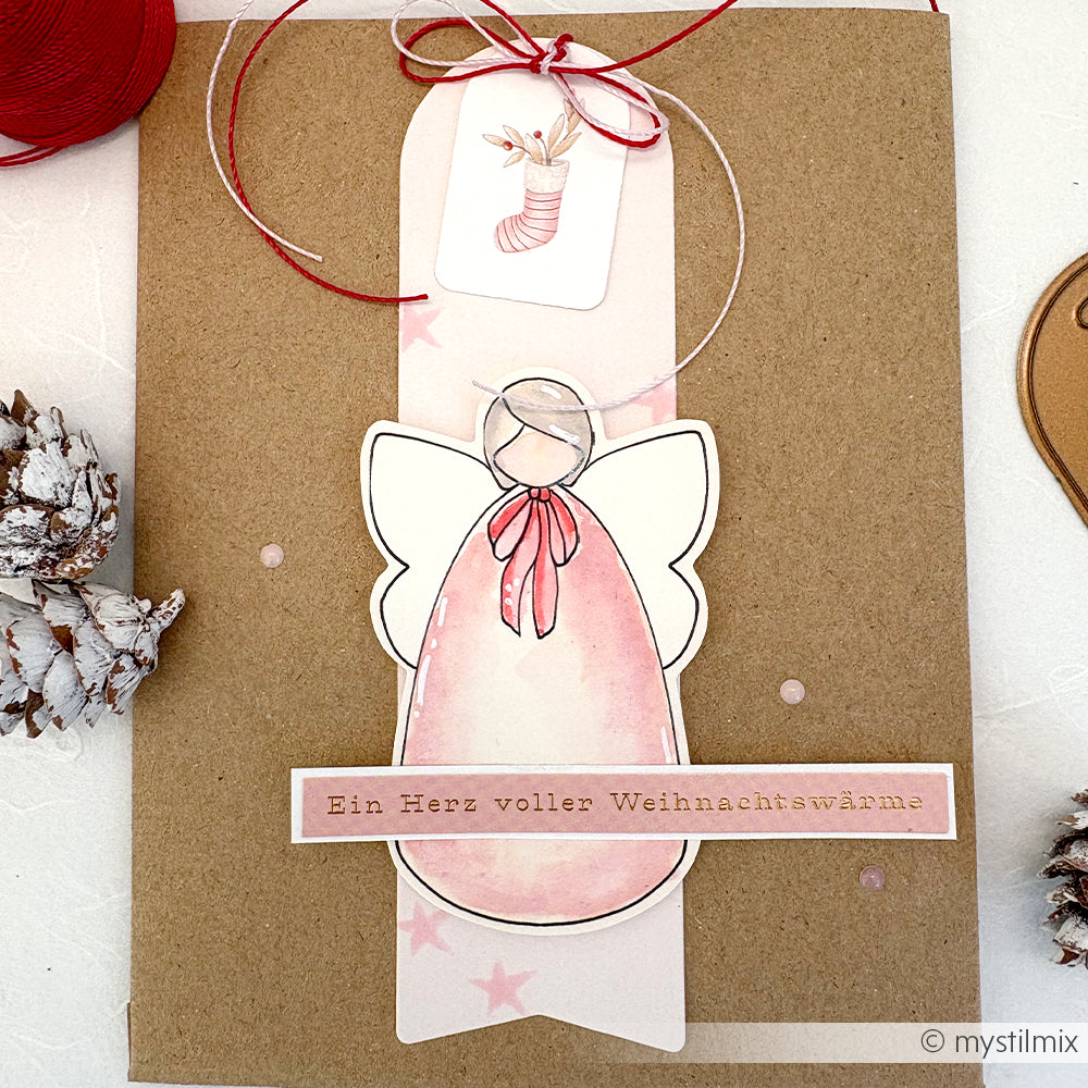Handgefertigte Weihnachtskarte von Alexandra Renke mit einem rosa Engel, deutschem Text, rotem Band und festlichen Tannenzapfen - eine einzigartige Ergänzung für Ihre Weihnachtsephemera oder perfekt für Papertie-Projekte.