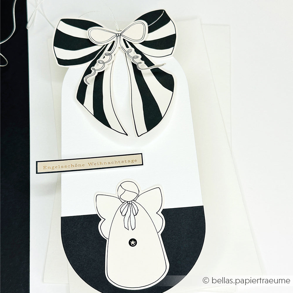Ein schwarz-weißer Geschenkanhänger von Alexandra Renke mit einer gestreiften Schleife und einem Engelsmotiv, beschriftet mit "Engelschöne Weihnachtstage" - ideal für Papertie-Projekte oder zum Hinzufügen charmanter Ephemera zu Ihren Weihnachtsgeschenken.
