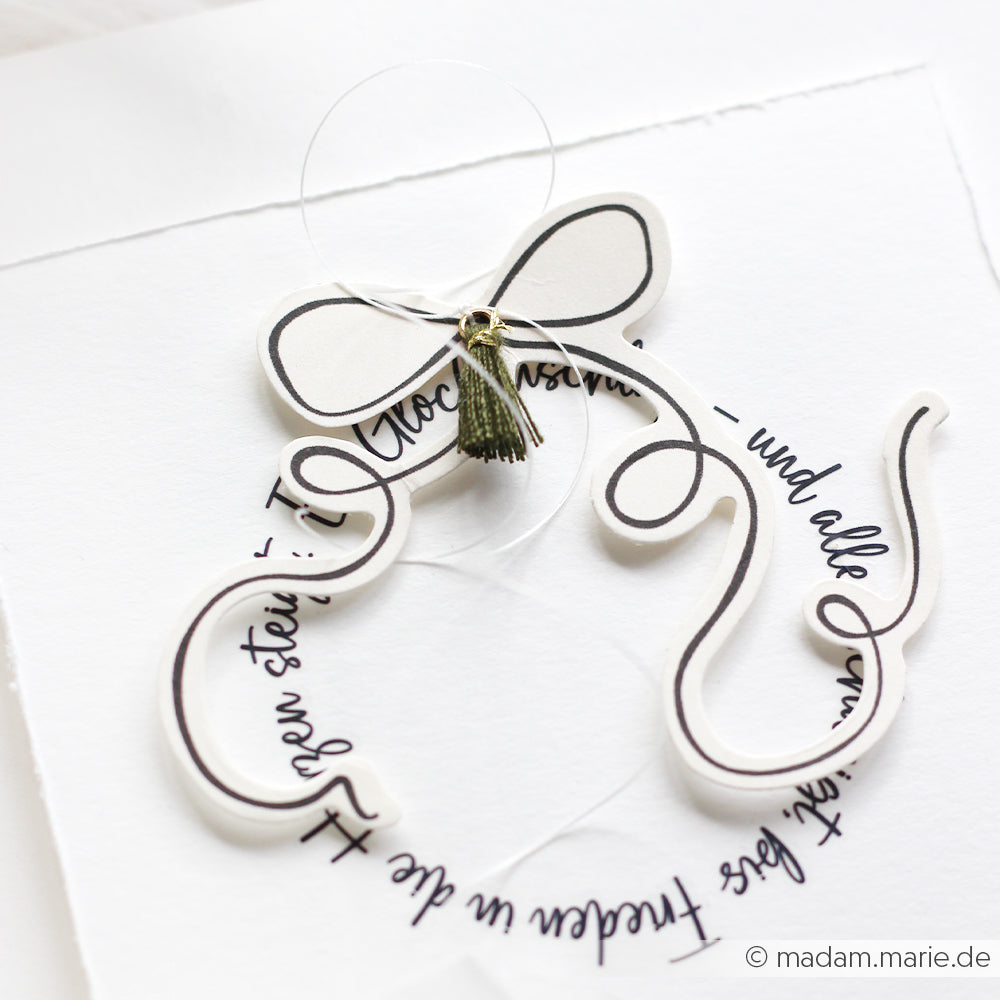 Weiße Karte von Alexandra Renke mit schwarzem Schriftzug, einer Papierschleife und einer grünen Quaste - ideal, um Ihre Papertie-Projekte aufzuwerten oder Ihrer Papierelemente-Kollektion ein einzigartiges Flair zu verleihen.