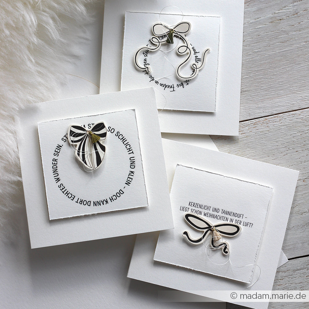 Drei weiße Alexandra Renke-Grußkarten mit Silberdrahtkunst, deutschem Text und dekorativem Faden auf einer weichen Oberfläche - einzigartige Designs, die Papierelemente mit zarten Ephemera für einen raffinierten Touch kombinieren.