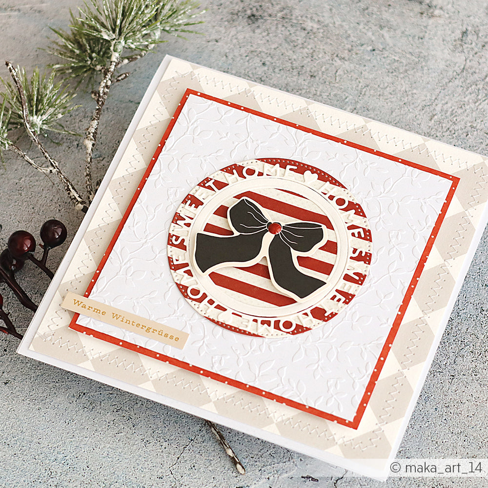 Handgemachte Wintergrußkarte von Alexandra Renke mit Papierelementen, einer schwarzen Schleife und einem rot-weiß gestreiften Hintergrund neben Tannen und Beeren.