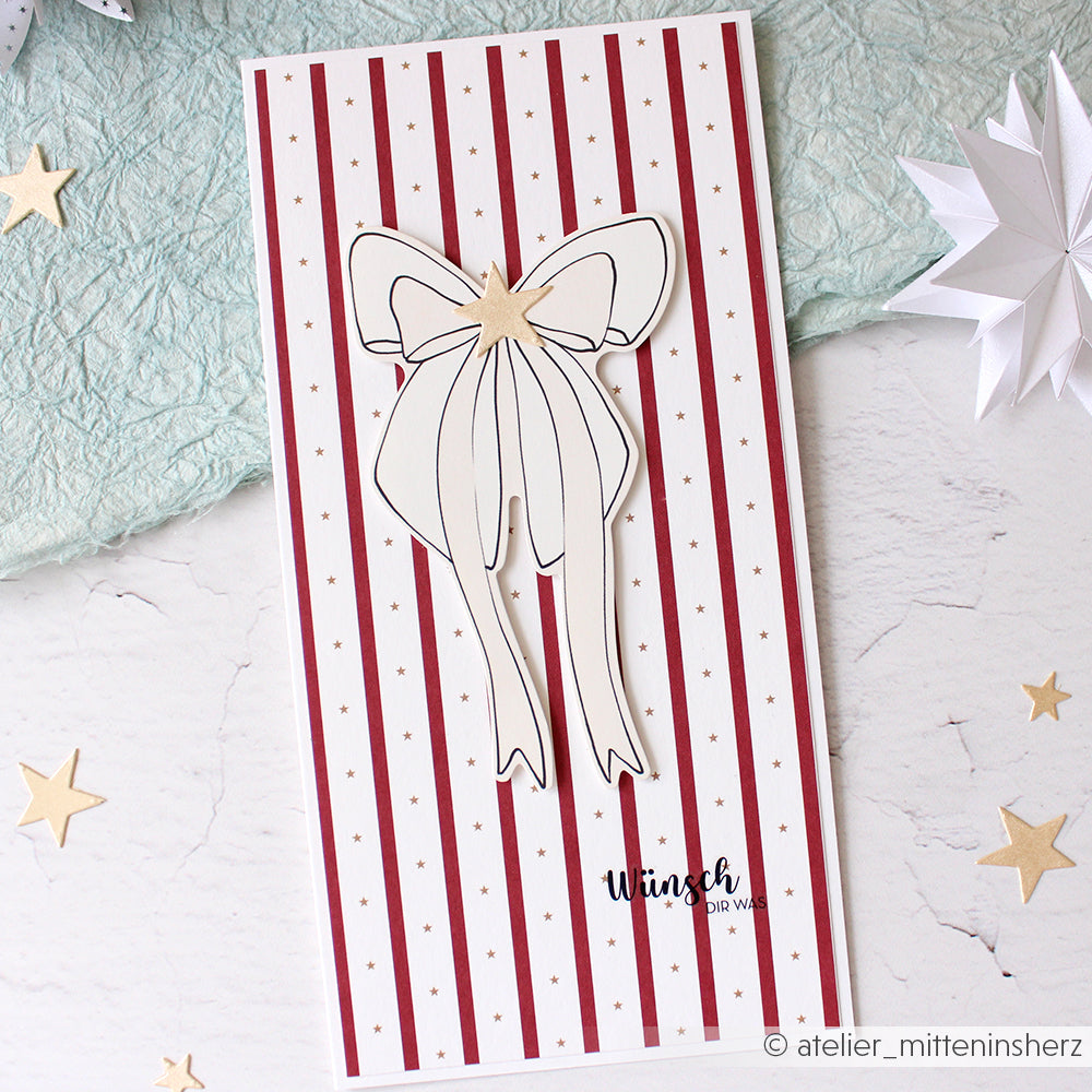 Rechteckige Karte von Alexandra Renke mit roten Streifen, einer großen weißen Schleife, einem goldenen Stern und dem Schriftzug "Wunsch" am unteren Rand - ideal für Papertie-Projekte oder zur Erweiterung Ihrer Sammlung um festliche Ephemera.