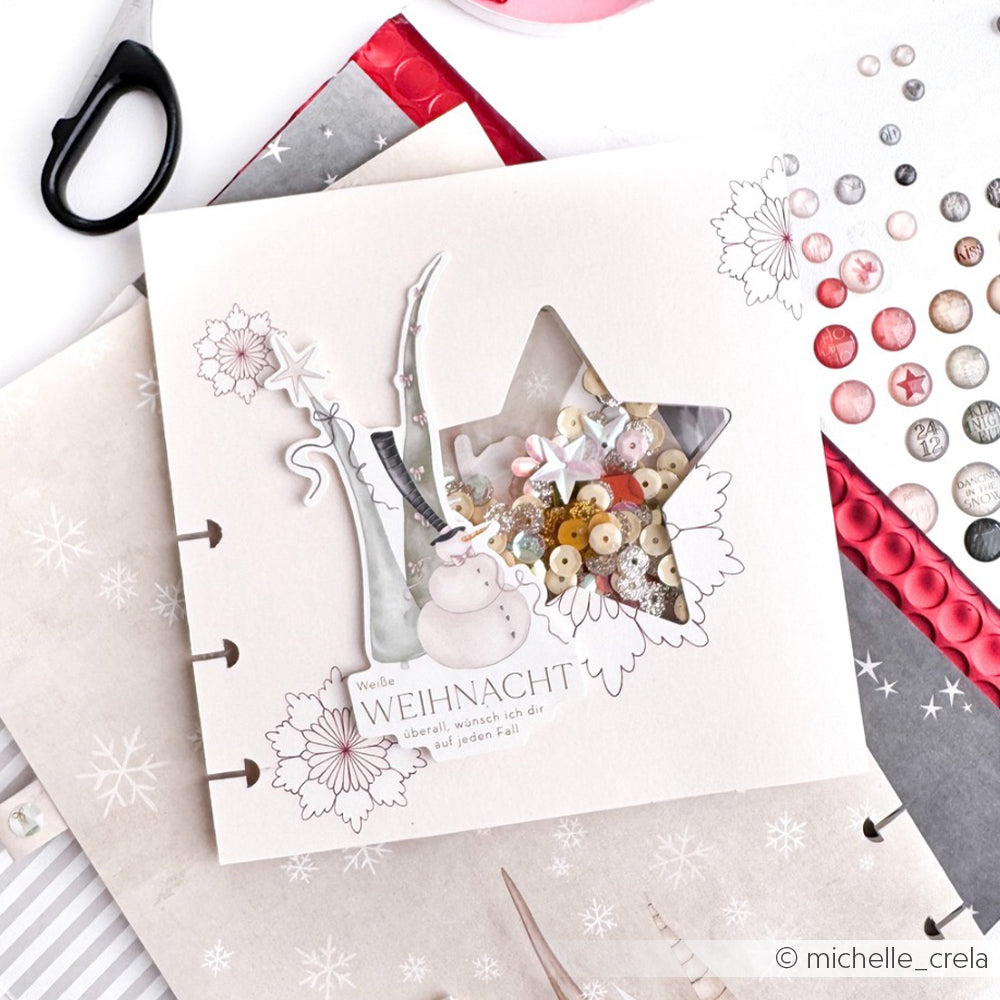 Handgefertigte Weihnachtskarte von Alexandra Renke mit sternförmigem Fenster, festlichen Papierelementen, Ephemera-Akzenten und Knöpfen im Innern, wunderschön auf einem weißen Tisch präsentiert.