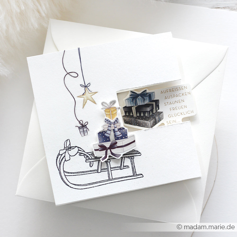Handgefertigte Karte von Alexandra Renke mit Schlitten, Geschenkboxen, Sternen und deutschem Text auf weißem Umschlag - ideal für Papertie-Projekte oder zur Erweiterung Ihrer Sammlung um festliche Ephemera.