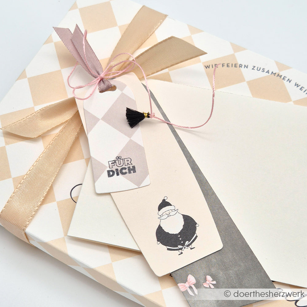Geschenk mit beigem Band, zwei Anhängern von Alexandra Renke - auf dem einen steht "Für Dich", auf dem anderen eine Weihnachtsmann-Illustration und eine rosa Schnur.