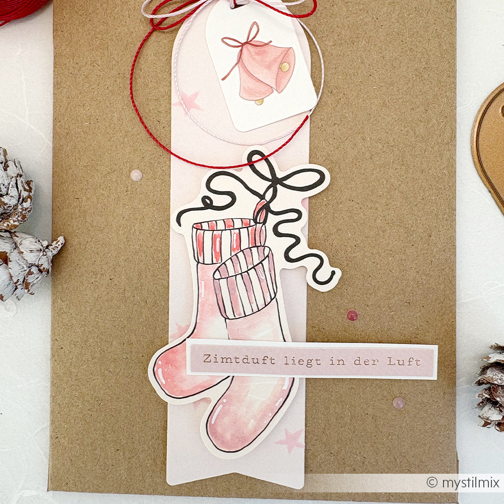 Handgefertigte Karte von Alexandra Renke mit rosa Weihnachtsstrümpfen, einem Glockenanhänger und deutschem Text: Zimtduft liegt in der Luft. Ideal für Papertie-Projekte oder zur Ergänzung Ihrer Weihnachtssammlung mit festlichen Ephemera.