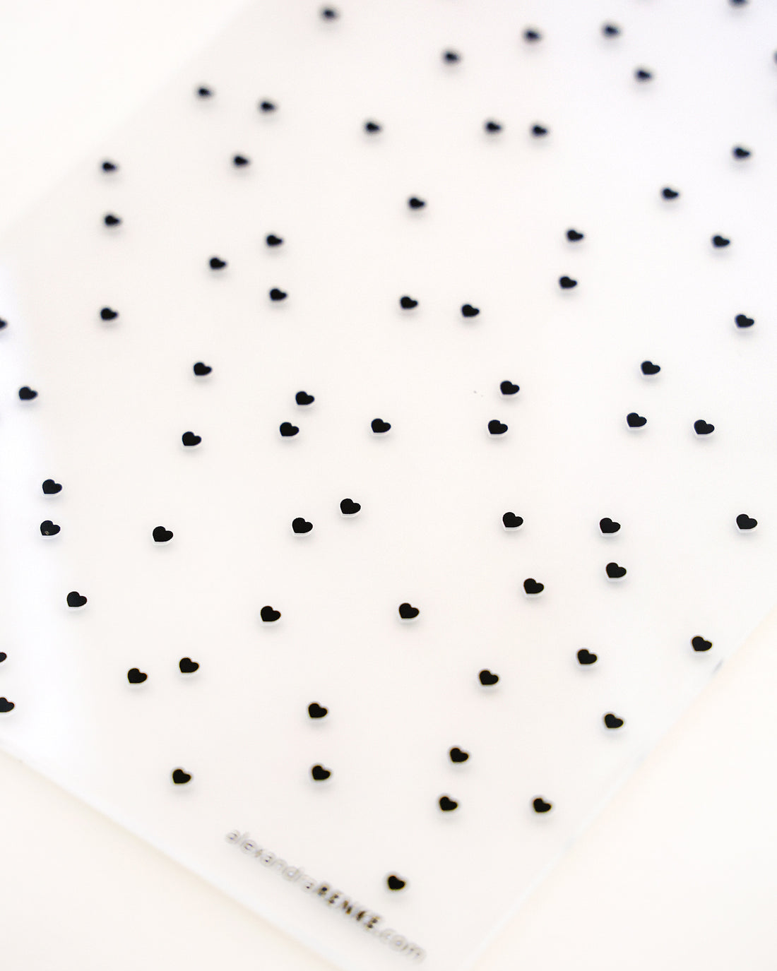 Blatt mit kleinen schwarzen Herzaufklebern, die in einem Raster auf weißem Hintergrund angeordnet sind.