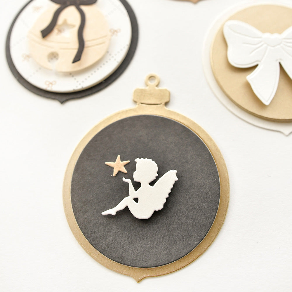 Goldfarbenes Ornament mit einer weißen Feensilhouette, die einen Stern hält, hergestellt mit Alexandra Renke DieCut Systeme und Motivstanze Mini Engel, umgeben von anderen dekorativen Ornamenten.