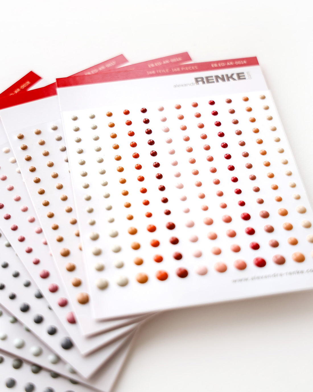 Bögen mit selbstklebenden Emaille-Punkten in verschiedenen Farben, die in ordentlichen Reihen auf weißen Karten angeordnet sind.