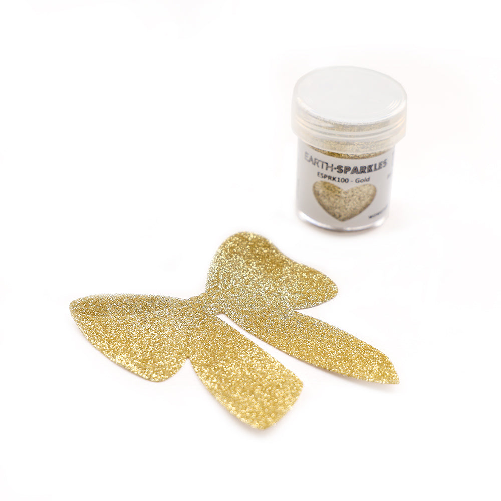 Eine Dose goldenes WOW Embossing Powder Bio Glitter mit der Aufschrift Earth-Sparkles steht neben einer ausgeschnittenen goldenen Glitzerschleife auf weißem Hintergrund, die ihre pflanzlichen Glitzer- und biologisch abbaubaren Eigenschaften zur Schau stellt.