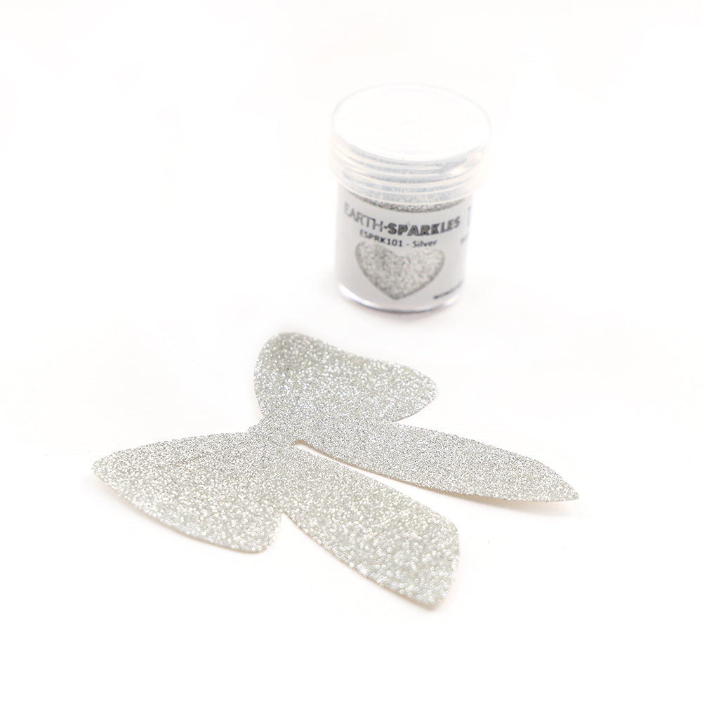 Eine kleine Dose WOW Embossing Powder Bio Glitter und eine silberne Glitzerschleife auf weißem Hintergrund, mit biologisch abbaubaren pflanzlichen Glitzerflocken für umweltfreundliches Funkeln.