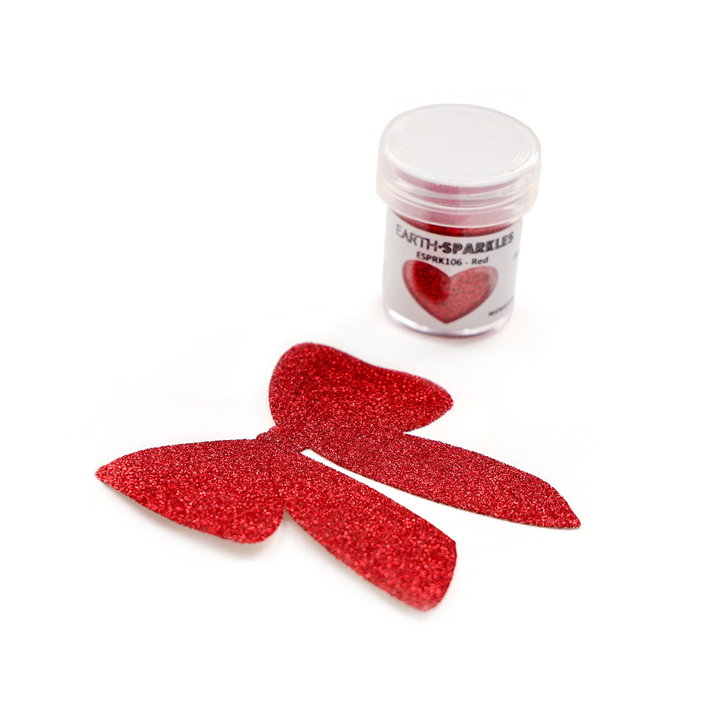Ein kleines Döschen WOW Embossing Powder Bio Glitter, hergestellt aus pflanzlichen Glitzerflocken, steht neben einer roten Glitzerschleife auf weißem Hintergrund.