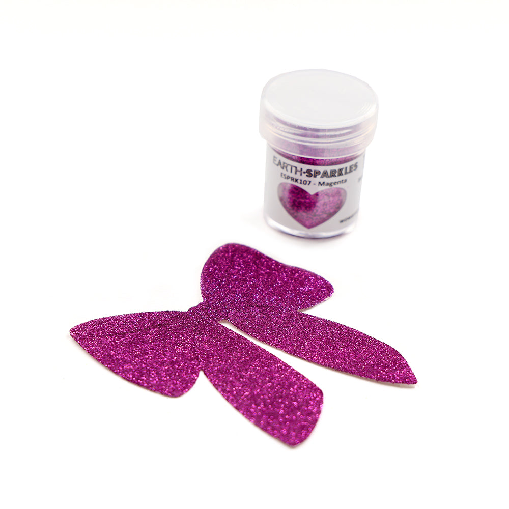 Eine Dose WOW Embossing Powder rosa Bio Glitter mit der Aufschrift Earth Sparkles steht neben einer großen, funkelnden rosa Schleife aus biologisch abbaubaren Glitzerflocken auf weißem Hintergrund.