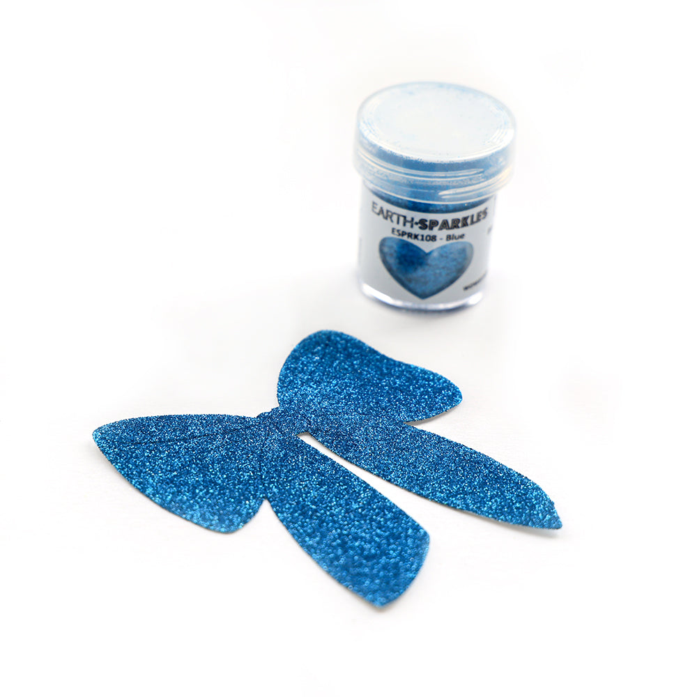 Eine Dose WOW Embossing Powder blue Bio Glitter steht neben zwei blauen Glitzerschleifen aus biologisch abbaubaren pflanzlichen Glitzerflocken auf weißem Hintergrund.