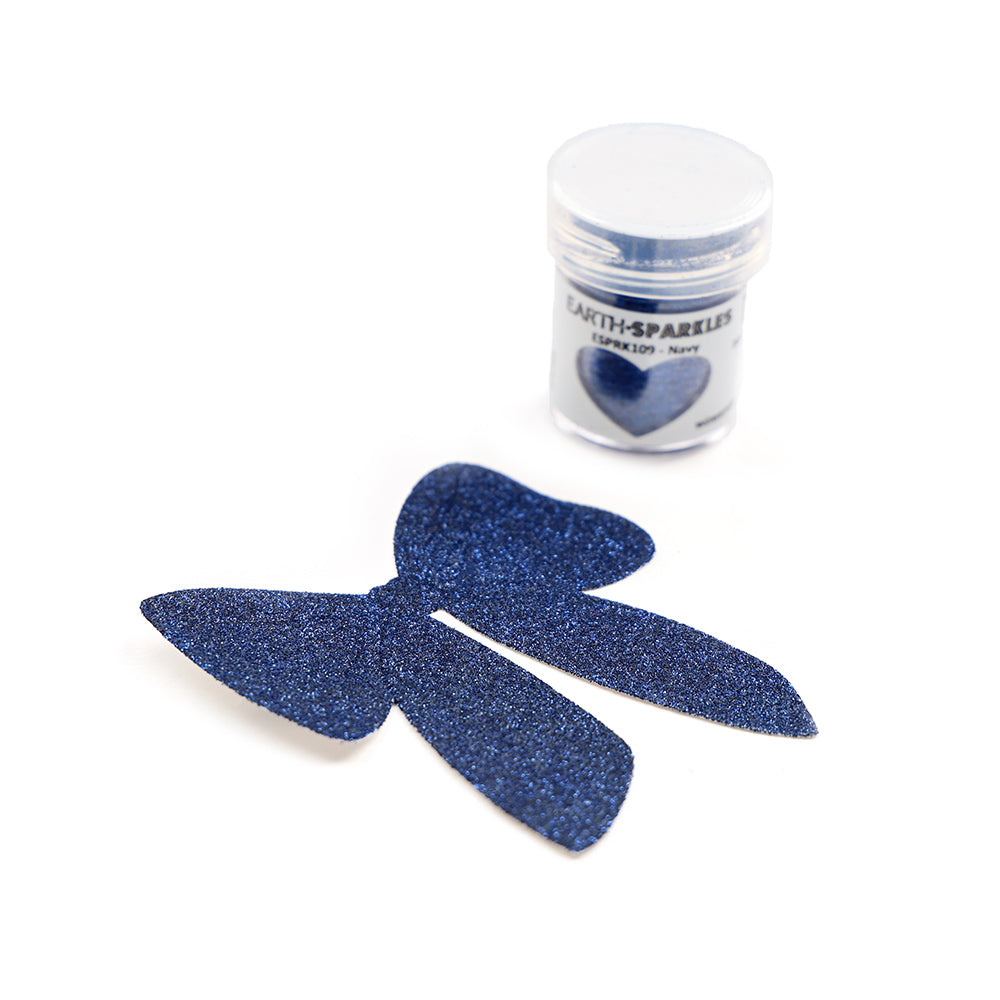 Kleines Döschen WOW Embossing Powder navy blue Bio Glitter neben einer ausgeschnittenen Schleifenform, die mit demselben navy blue, biologisch abbaubaren Glitter überzogen ist.
