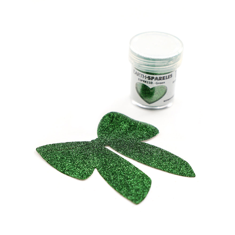 Eine Dose WOW Embossing Powder Bio Glitter steht neben einer großen, grünen Glitzerschleife auf weißem Hintergrund.