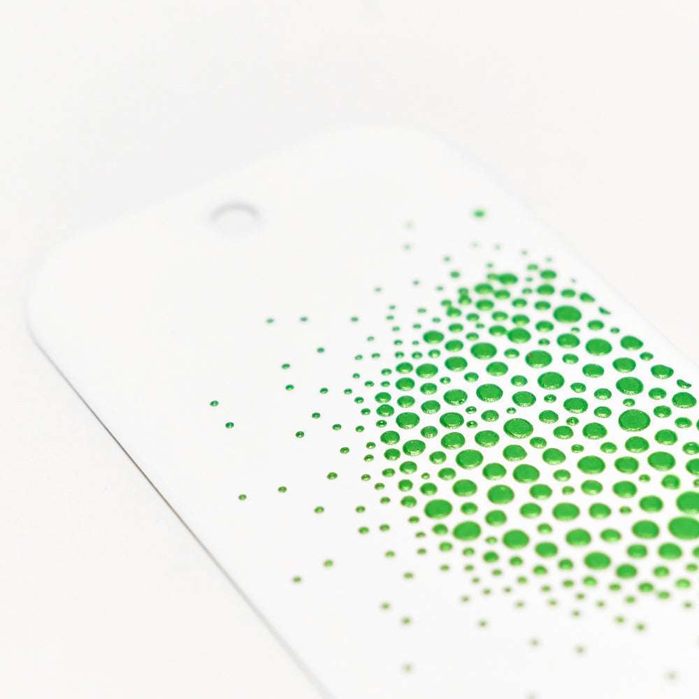 Auf einer weißen Karte befinden sich grüne Punkte unterschiedlicher Größe, die auf einer Seite konzentriert sind und mit der Schablonenbutter von The Crafters Workshop für einen lebendigen Mixed-Media-Effekt gesorgt haben.