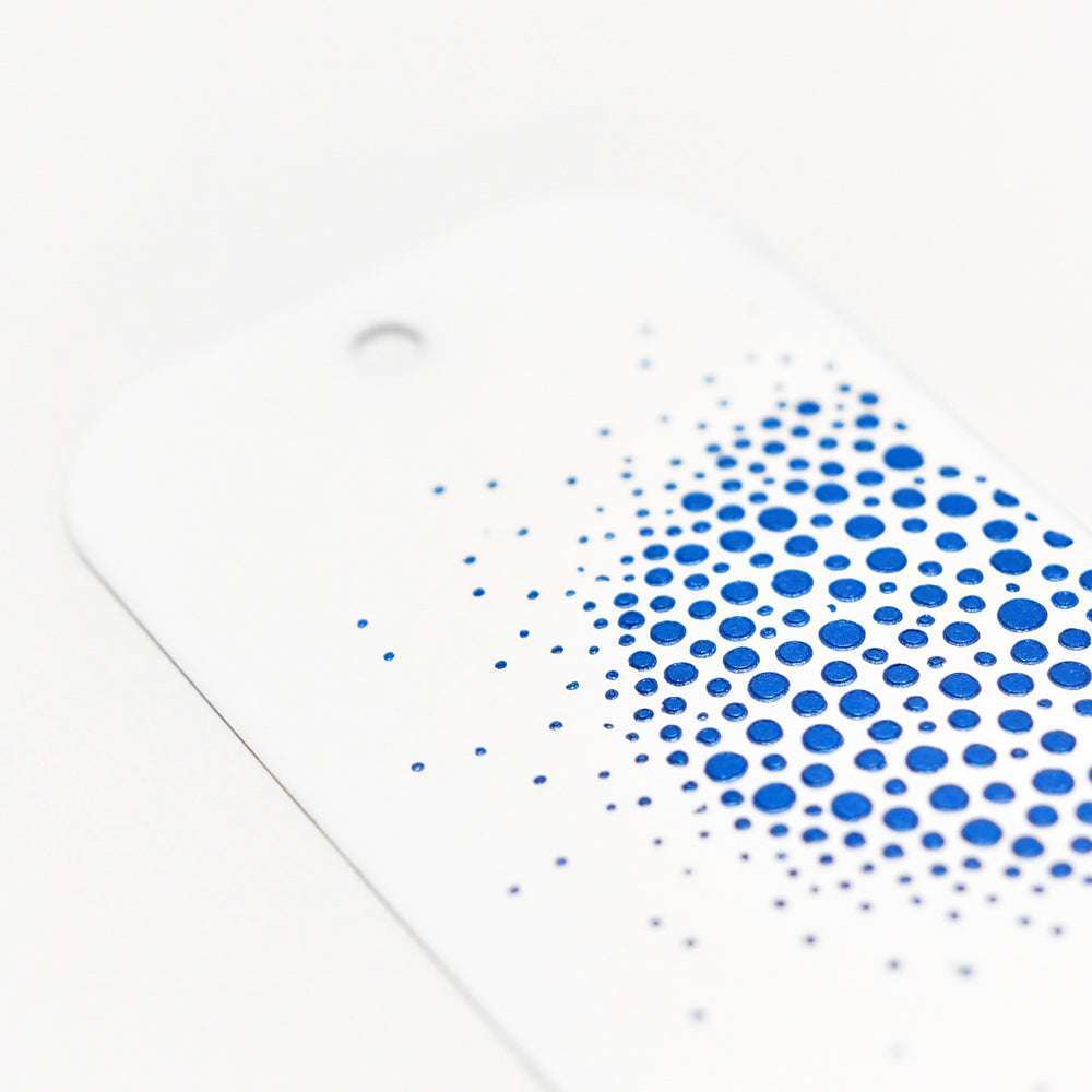 Weißer Anhänger mit einem Loch oben, verziert mit blauen Punkten in einem Farbverlauf - ideal für Mixed-Media-Techniken oder zum Hinzufügen von Texturen mit Stencil Butter. Von The Crafters Workshop.