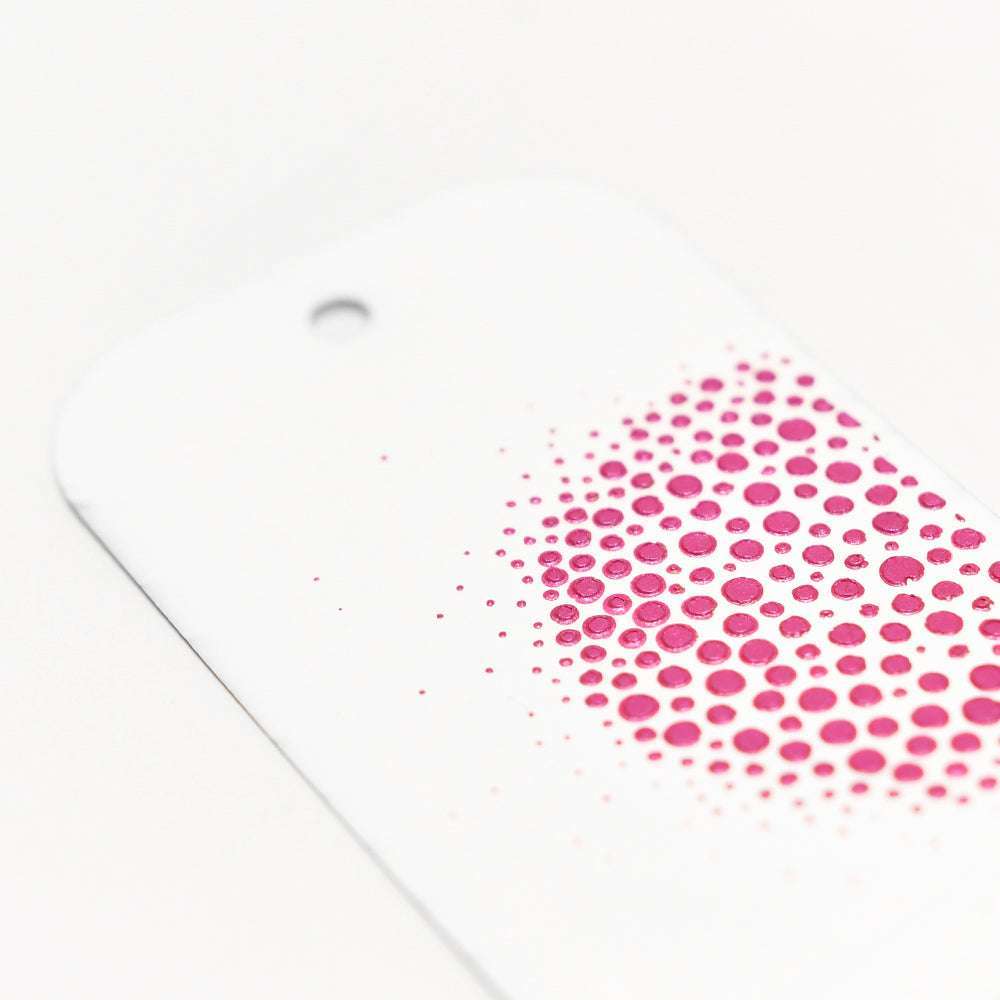 Ein weißer Anhänger von The Crafters Workshop mit einem Loch und einem Farbverlauf aus rosa Punkten auf der rechten Seite, der mit Mischtechniken erstellt wurde.