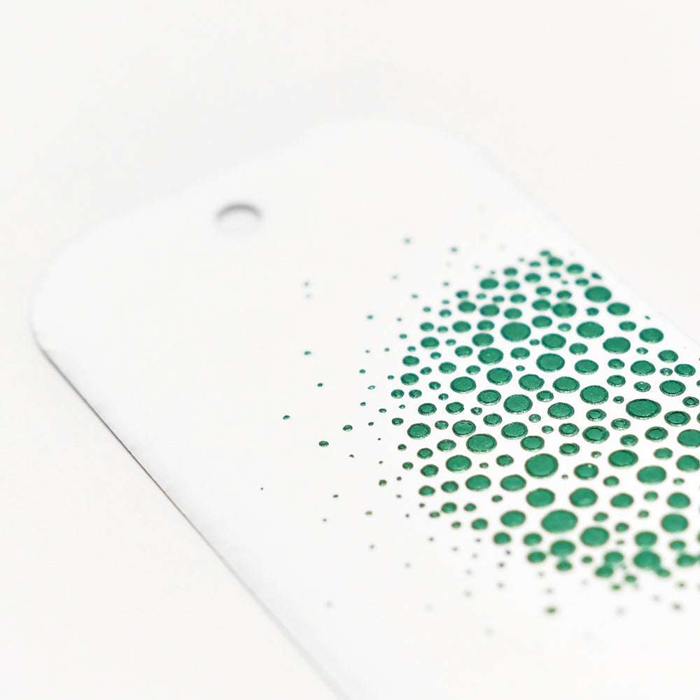 Weiße Karte von The Crafters Workshop mit erhabenen grünen Punkten aus Modellierpaste, die sich nach außen ausbreiten, und einem gestanzten oberen Loch - ideal für Mixed-Media-Projekte.