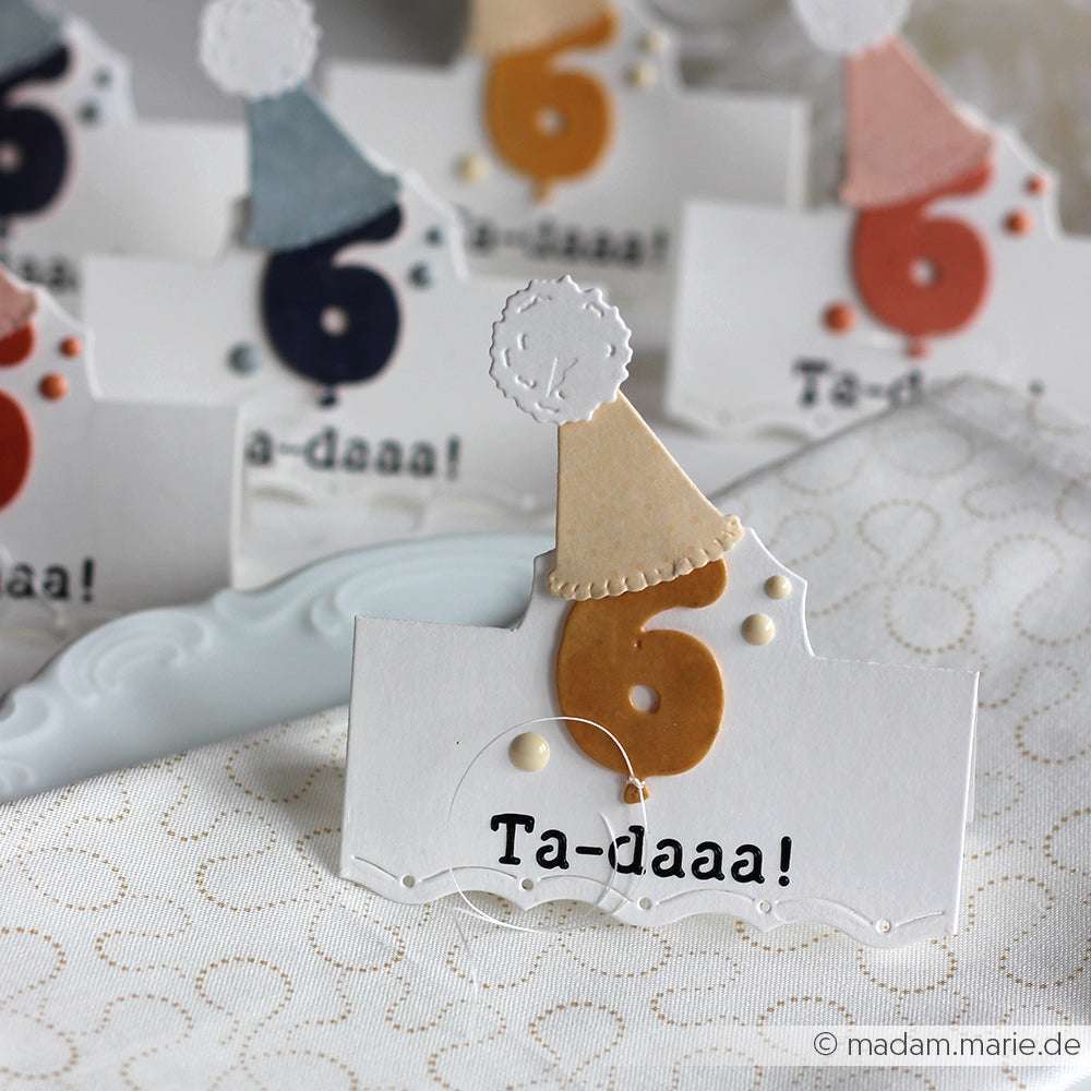 Der Crafters Workshop: Weiße Karte mit einer ausgeschnittenen Nummer 6, einem Partyhut und dem Text "Ta-daaa!" - ideal für die Präsentation von Stencil Butter oder Modellierpaste auf Mixed Media Boards.