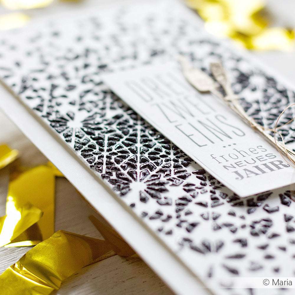 Nahaufnahme einer schwarz-weißen Weihnachtskarte von The Crafters Workshop mit deutschem Text, Goldfolienakzenten und Mixed-Media-Techniken für zusätzliche Textur und Dimension.