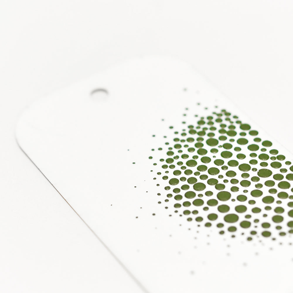 Ein weißer Anhänger von The Crafters Workshop ist mit einer Gruppe grüner Punkte versehen, die an den Rändern verblassen - ideal, um Ihrem nächsten Mixed-Media-Projekt mit Modellierpaste Dimension oder mit Stencil Butter lebendige Farbe zu verleihen.