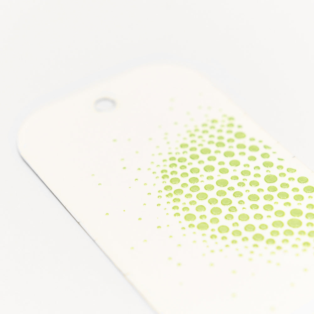 Ein weißer Anhänger von The Crafters Workshop mit einem Loch und grünen Punkten, die seitlich auslaufen. Ideal, um mit Stencil Butter Mixed-Media-Effekte zu erzielen.