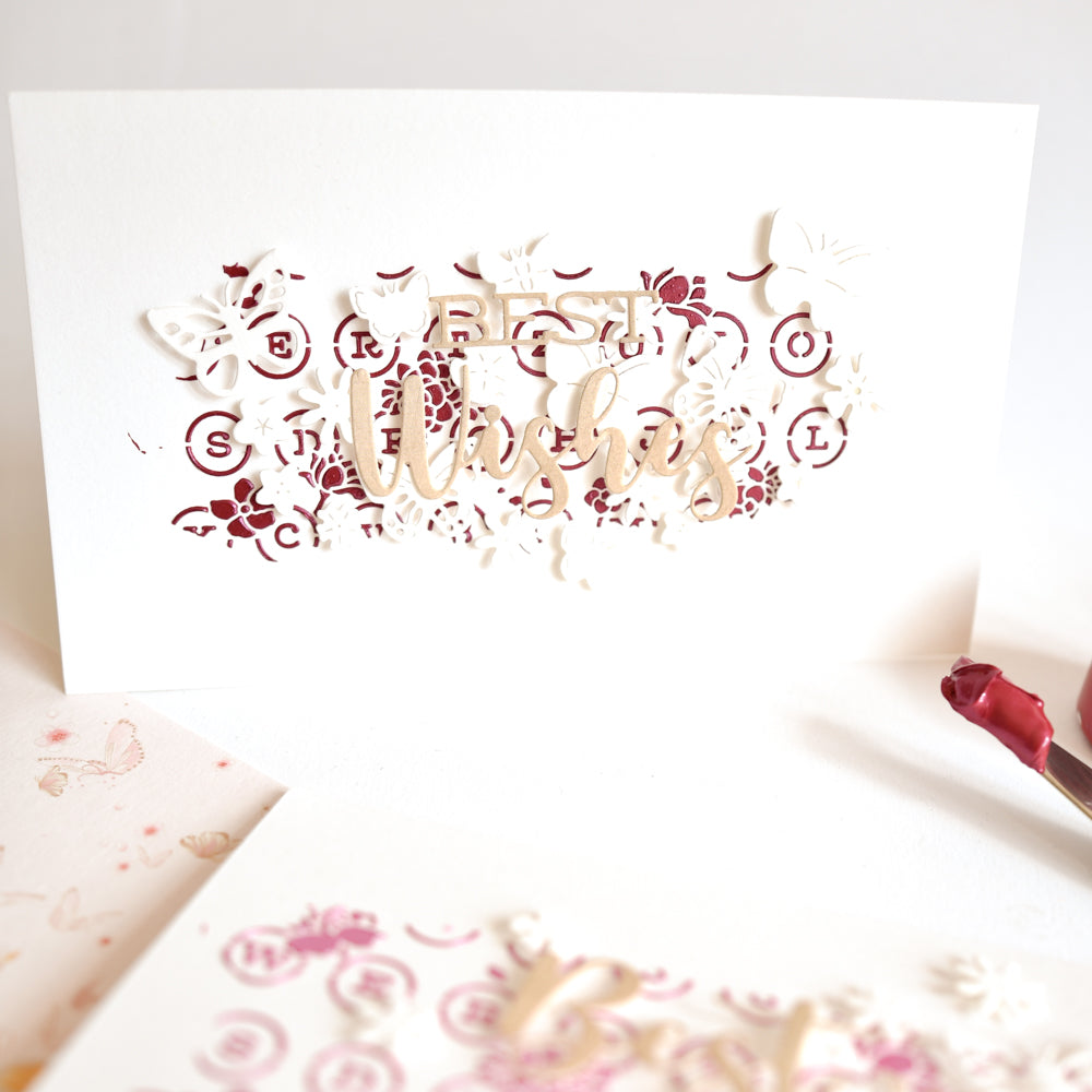 Handgefertigte „Best Wishes“-Karte mit filigranen Schmetterlings- und Blumenausschnitten auf weiß-rosa Hintergrund, wunderschön akzentuiert durch Mixed-Media-Techniken unter Verwendung von Produkten von The Crafter’s Workshop sowie zarten Akzenten aus Modellierpaste für zusätzliche Struktur.