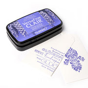 Ein blaues Tsukineko VersaFine Clair Pigmenttintenkissen mit einem weißen Anhänger, der mit blauem Blumen- und Dekotext bestempelt ist - ideal zum Stempeln feiner Details.