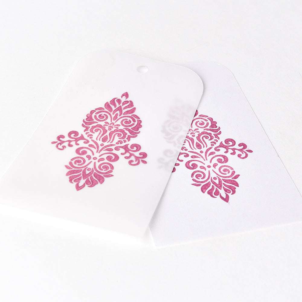 Zwei Anhänger mit verschlungenen rosa Blumenmustern - ein durchscheinend über weiß - veredelt mit Tsukineko Versa Magic Stempelkissen für glatte, lebendige Farben auf glattem Papier.