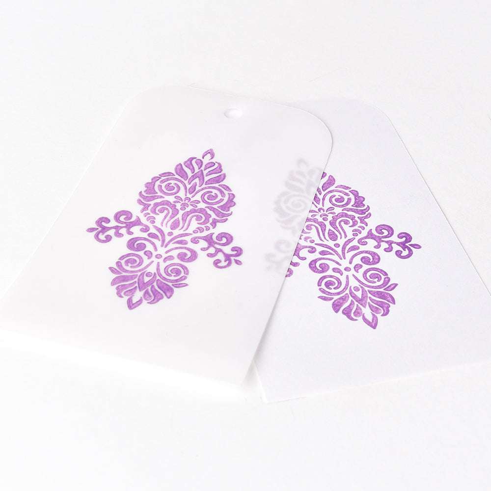 Zwei dekorative Anhänger mit verschlungenen lila Mustern - einer einfarbig, einer mit durchscheinendem Papier - sind wunderschön gestempelt mit der Tsukineko Versa Magic Stempelkissen Pigment-Tinte, ideal für glattes Papier.