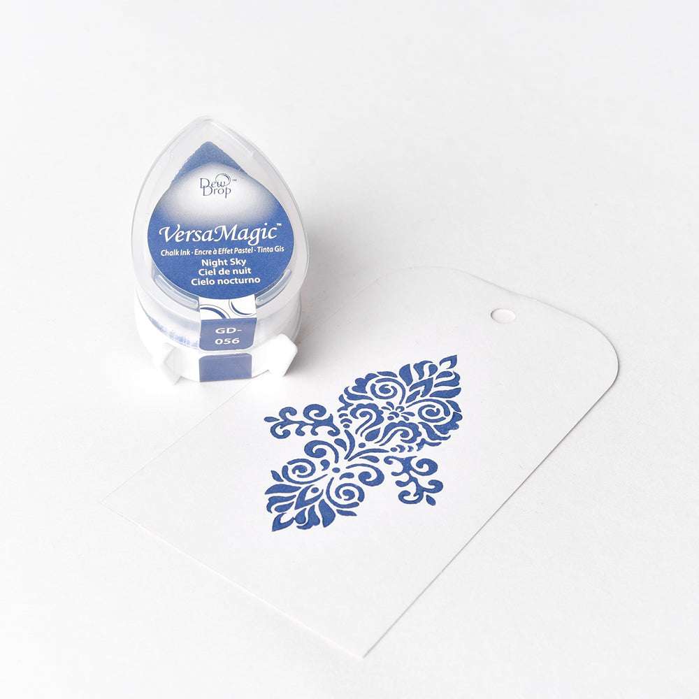 Ein blaues Stempelkissen von Tsukineko in kleiner Tropfenform und ein weißer Anhänger mit blauem Blumenmuster, gestempelt mit wasserbasierter Pigment-Tinte wie Versa Magic Stempelkissen.