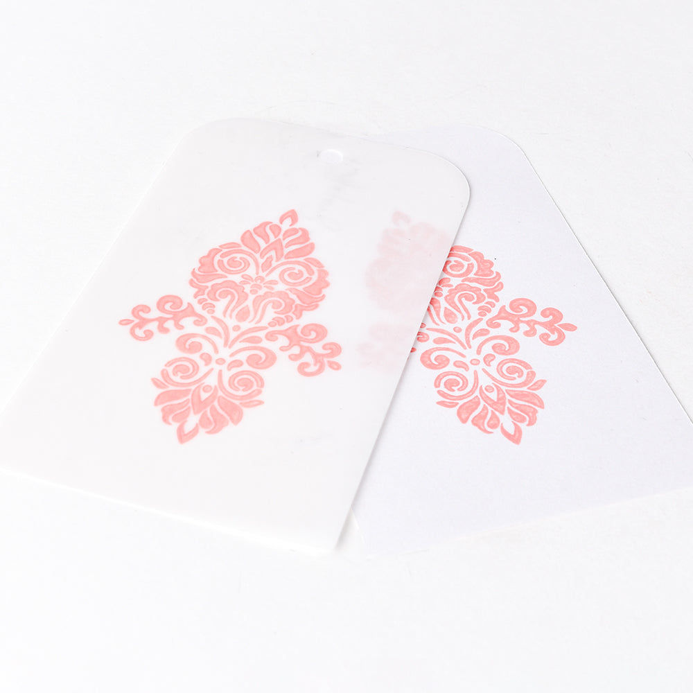 Zwei weiße Karten mit verschnörkelten rosafarbenen Blumenmustern, hergestellt mit Tsukineko Versa Magic Stempelkissen Pigment-Tinte, eine leicht überlappend auf weißem Hintergrund für schöne Stempelergebnisse.