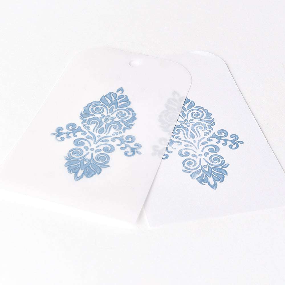 Zwei Anhänger mit verschnörkelten blauen Motiven - einer auf weißem Karton, einer auf halbtransparentem Pergament. Ideal für die Verwendung mit Tsukineko Pigment-Tinte oder Versa Magic Stempelkissen für gestochen scharfe, elegante Ergebnisse.