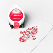 Tsukineko Memento Stempelkissen "Love Letter" neben einem weißen Anhänger mit roter Verzierung - ideal für gestochen scharfe Abdrücke und hochpigmentierte Farben.